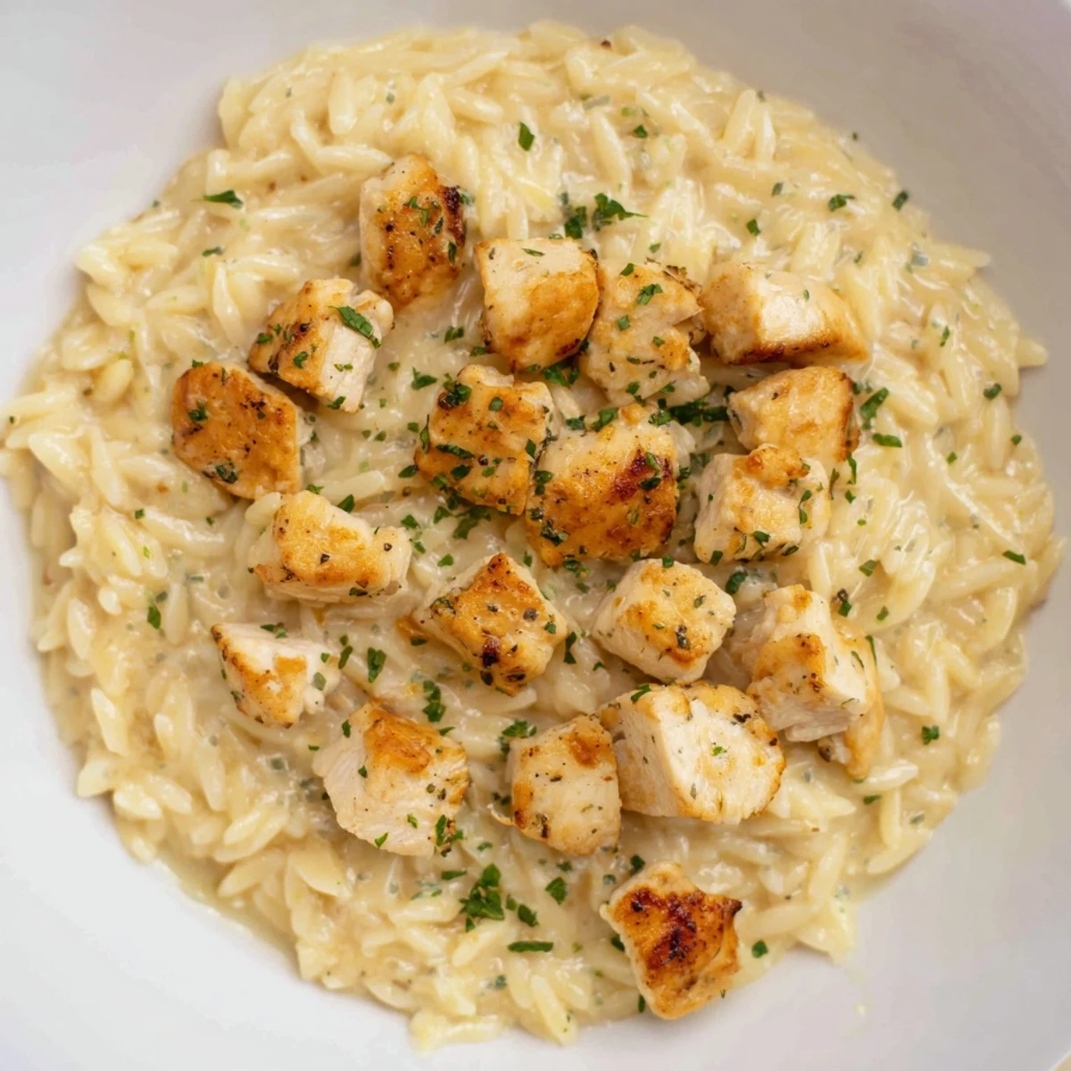 This One-Pot Cajun Chicken Alfredo Orzo features a vibrant swirl of parsley garnishing the dish.
