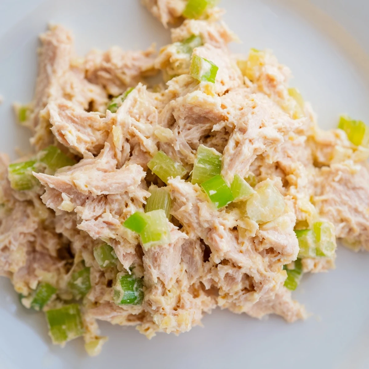A sandwich filled with Spicy Zesty Tuna Salad sits on a wooden board, showcasing the textured tuna and crisp lettuce between toasted whole wheat bread slices.  