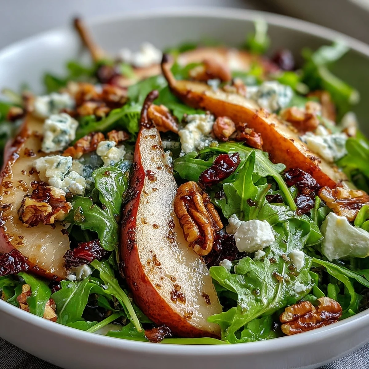 Fresh arugula and sliced ripe pears topped with creamy crumbled blue cheese and toasted walnuts in a salad bowl.