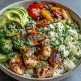 A vibrant Cauliflower Rice Bowl topped with creamy avocado slices, cherry tomatoes, and fresh cilantro.