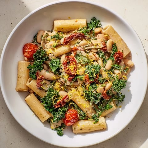 Steaming bowl of Healthy Tuscan White Bean & Kale Christmas Pasta, garnished with lemon zest and cheese.