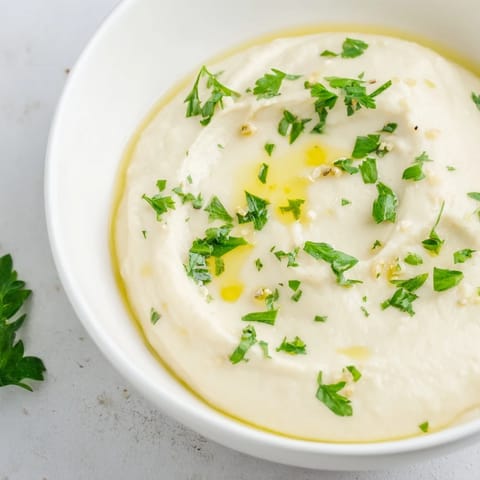 A close-up of smooth, blended White Bean Dip topped with fresh herbs, ready to serve.