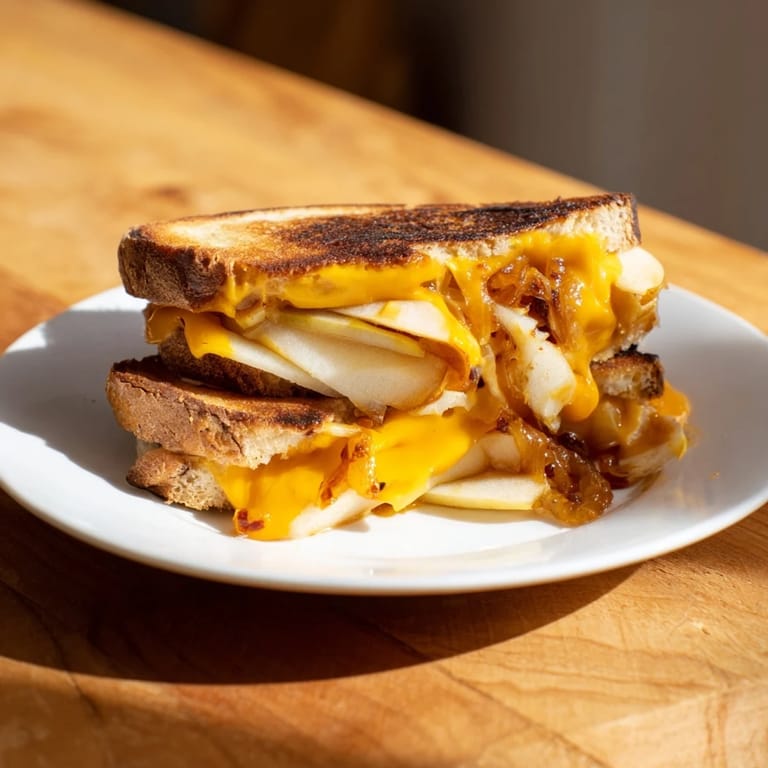A close-up shot of the melty Caramelized Onion, Apple & Cheddar Grilled Cheese sandwich on a plate.