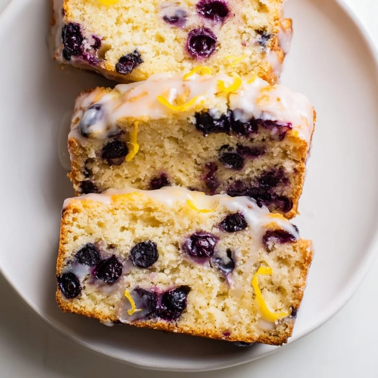 A slice of tender Lemon Blueberry Yogurt Loaf, topped with glaze and bursting with blueberries.