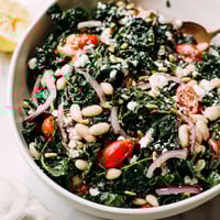 Fresh kale and creamy white beans tossed in a bright lemon-garlic dressing, topped with cherry tomatoes and sunflower seeds in a rustic bowl.
