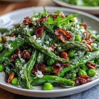 Vibrant shaved asparagus and pea salad with lemon dressing, fresh spring greens, and Parmesan shavings in a bright bowl.