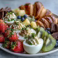 Easter brunch board with deviled eggs, fruit, and pastries on a rustic wooden board.